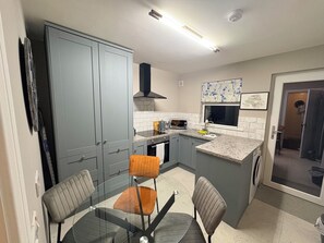 A compact kitchen with grey cabinets, a microwave, and a sink. There are two chairs and a glass table. - Cosy 2 bedroom House close to beach, shops, bus/train, and Royal Portrush Golf (Portrush)