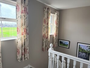 A room with floral curtains, a window with a view of a green field, and two framed pictures on the wall. - Cosy 2 bedroom House close to beach, shops, bus/train, and Royal Portrush Golf (Portrush)