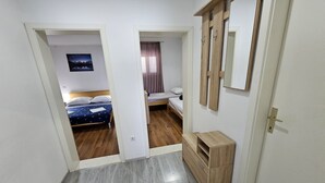 Ein schmaler Flur, der zu zwei Schlafzimmern mit Holzboden, einer kleinen Holzkommode und einem Spiegel an der Wand führt.