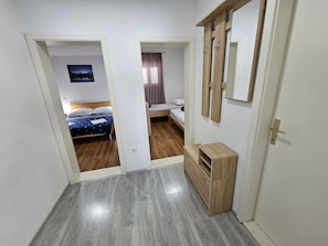 Un corridoio stretto che conduce a due camere da letto con pavimento in legno, un piccolo armadietto in legno e uno specchio appeso al muro.