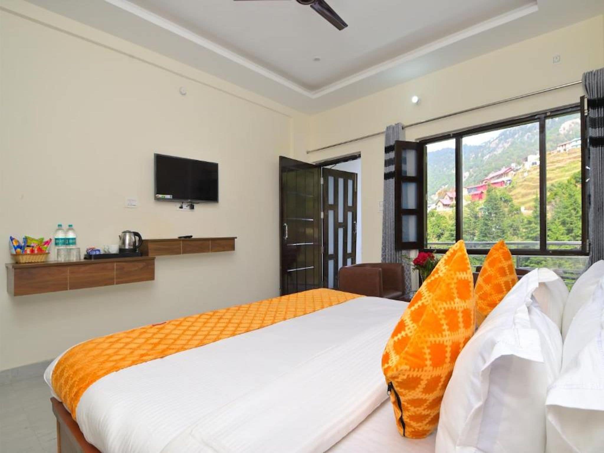 A hotel room with a bed, a TV, a window with a view, and a ceiling fan.