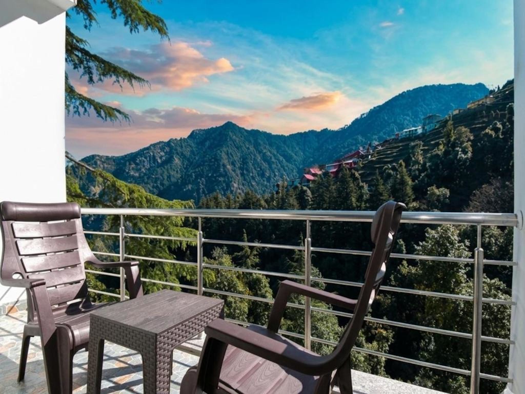 A balcony with two chairs and a table, overlooking a mountainous landscape with a clear sky.