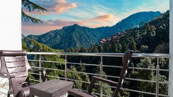 A balcony with two chairs and a table, overlooking a mountainous landscape with a clear sky.