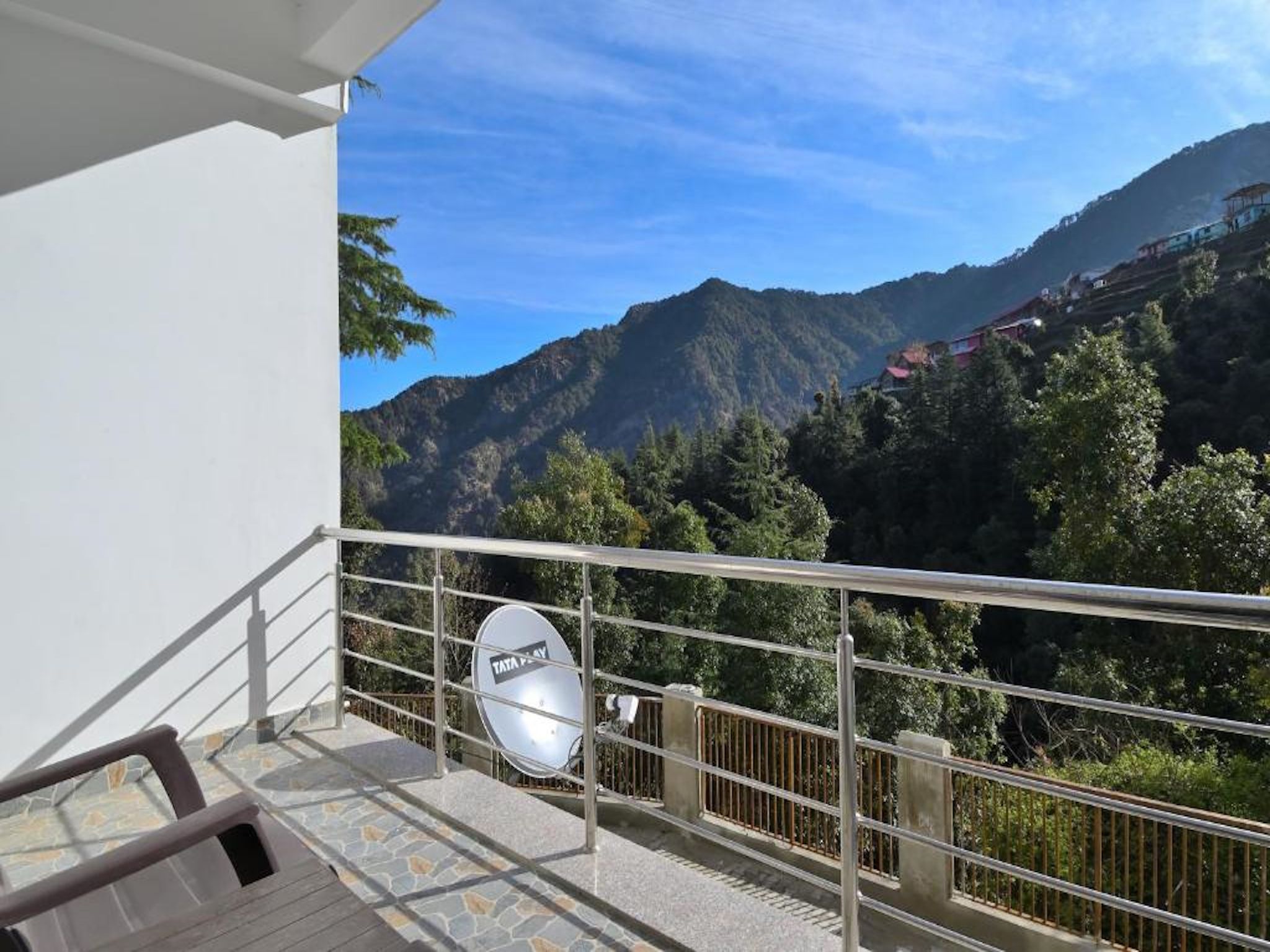 A balcony with a view of a mountainous landscape, a satellite dish, and a railing.