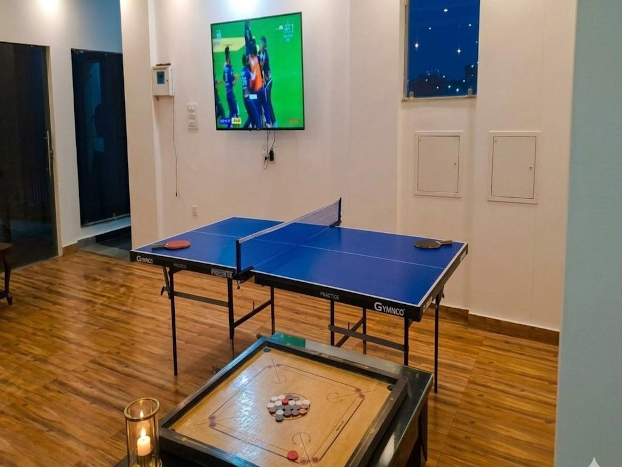 Ein Raum mit zwei Tischtennisplatten, einem an der Wand befestigten Fernseher und einem Tisch mit Bällen und Schläger.