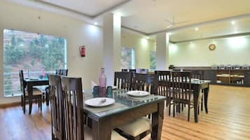A dining area with wooden tables and chairs, a fire extinguisher on the wall, and a view of the outdoors through large windows.