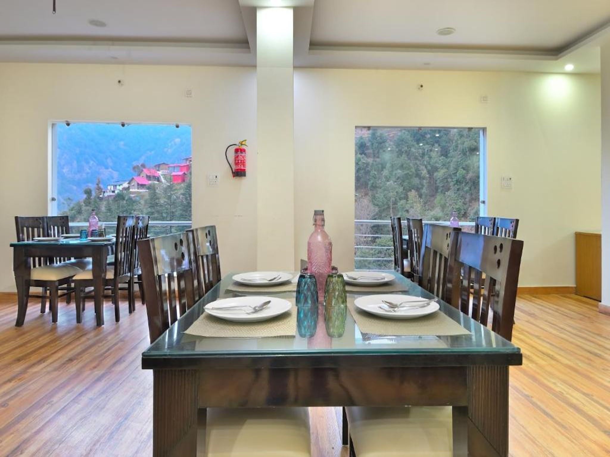 A dining area with a glass table, wooden chairs, and a view of a mountainous landscape through large windows.