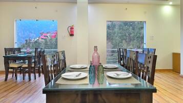 A dining area with a glass table, wooden chairs, and a view of a mountainous landscape through large windows.