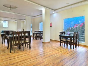 Un comedor amplio con suelo de madera y mesas, ventanas grandes con vista a un paisaje montañoso y un extintor de incendios fijado en la pared.