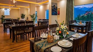 A dining area with tables set for two, wooden flooring, and a view of mountains through a window. - LA Riqueza Dhanolti (Dhanolti)
