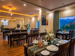 A dining area with tables set for two, wooden flooring, and a view of mountains through a window. - LA Riqueza Dhanolti (Dhanolti)