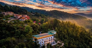 A multi-story building with a green roof, surrounded by dense forest, and a mountainous backdrop. - LA Riqueza Dhanolti (Dhanolti)