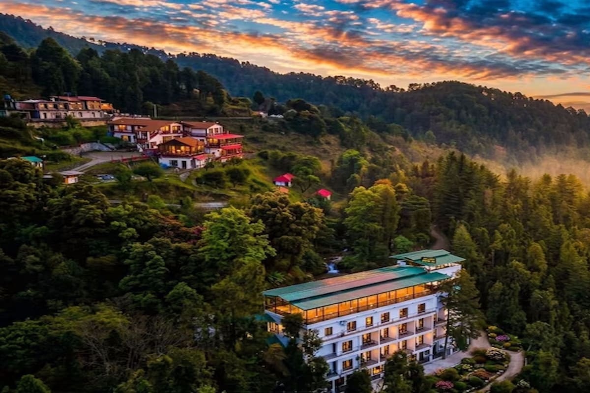 A multi-story building with a green roof, surrounded by dense forest, and a mountainous backdrop.