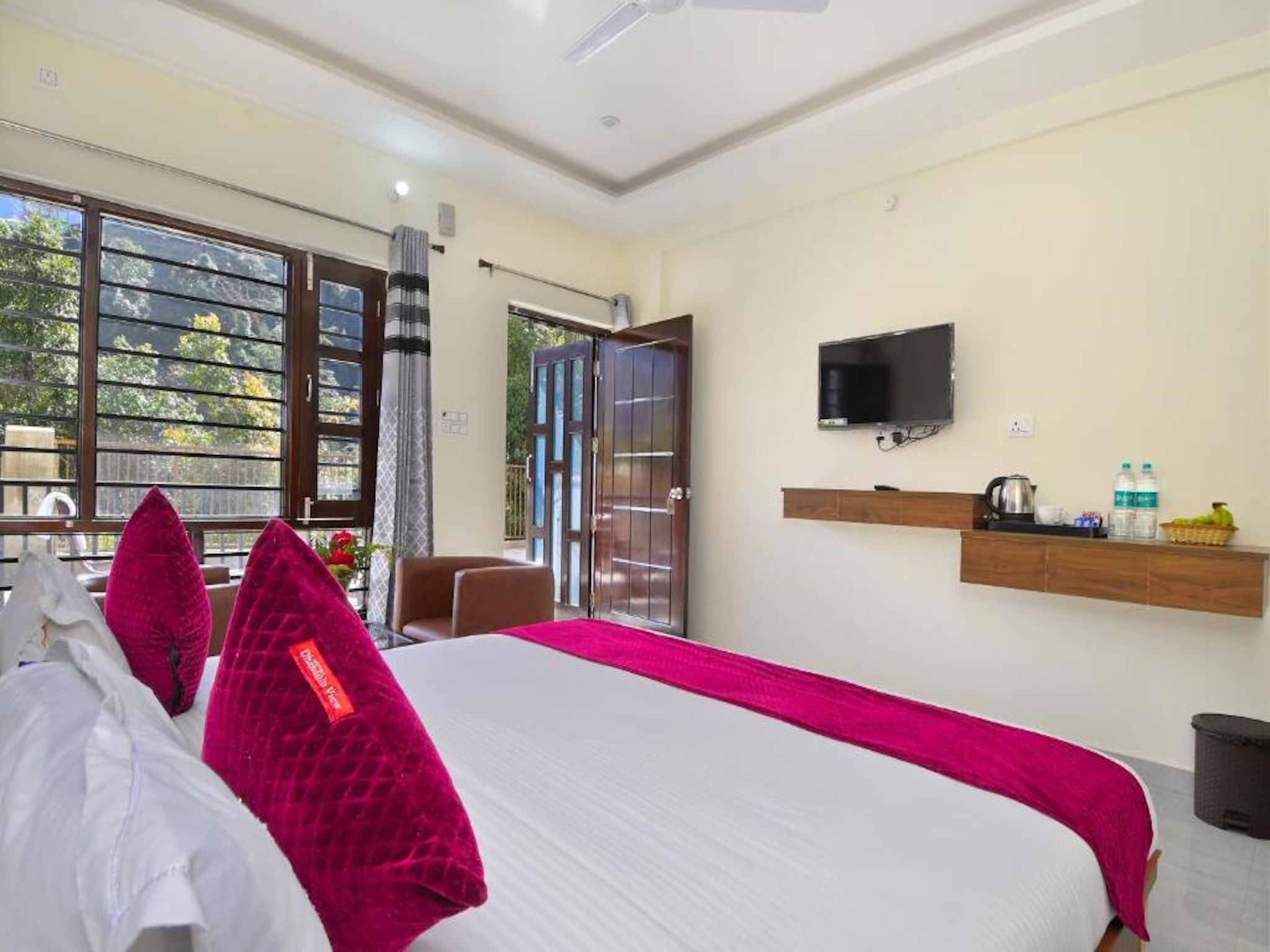 A hotel room with a bed, a television, a window with a view, and a door leading outside.