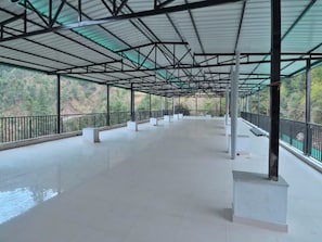An empty covered walkway with a metal roof and railings, surrounded by greenery. - LA Riqueza Dhanolti (Dhanolti)