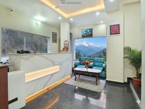 A modern reception area with a marble reception desk, a sofa with a mountain view, and a ceiling fan. - LA Riqueza Dhanolti (Dhanolti)