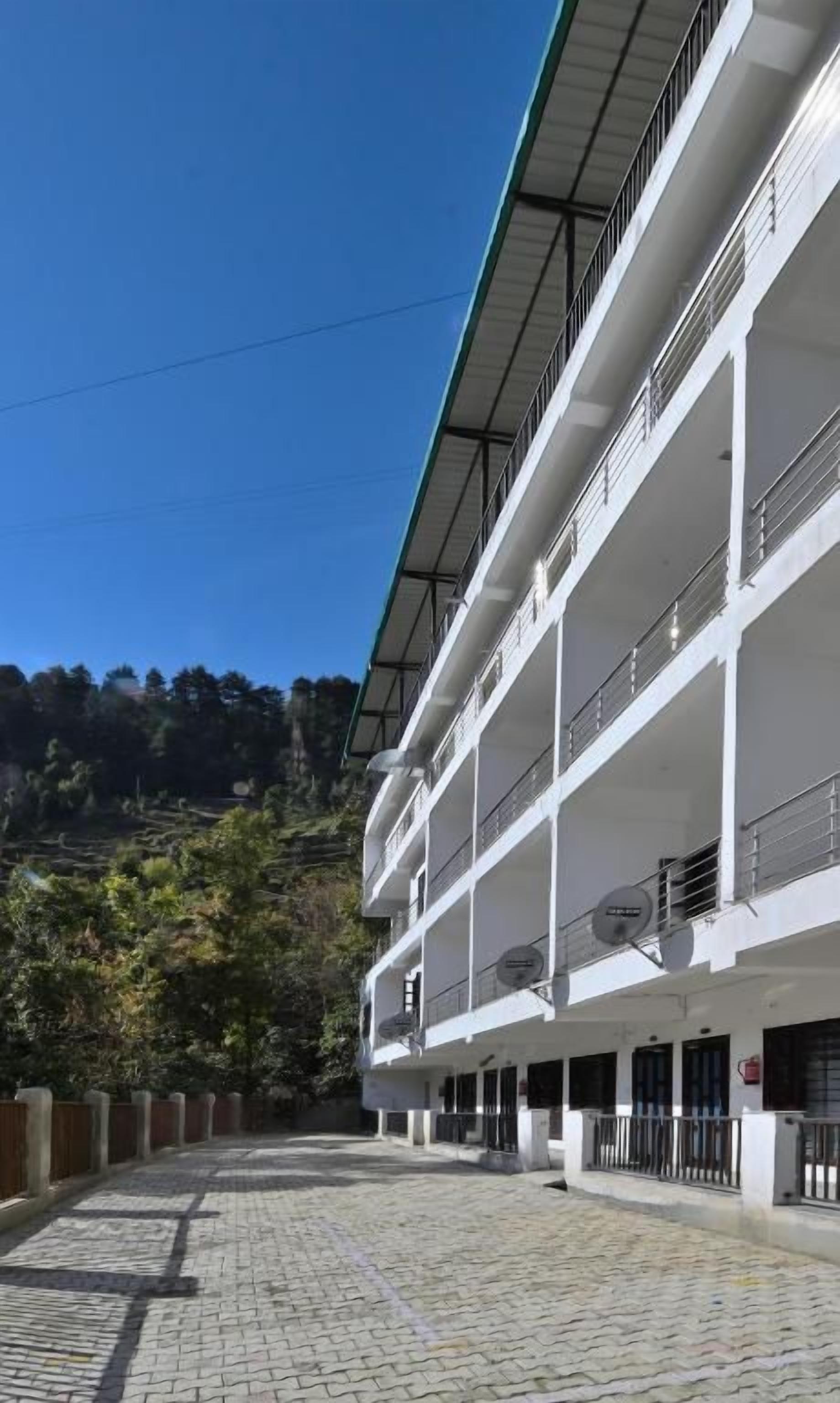 Un edificio de varios pisos con balcones, un patio empedrado y montañas al fondo.