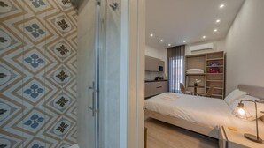 A modern bedroom with a bed, bedside table, and a desk with a lamp. - Urban Vibe 3 apartment (Kirkop)