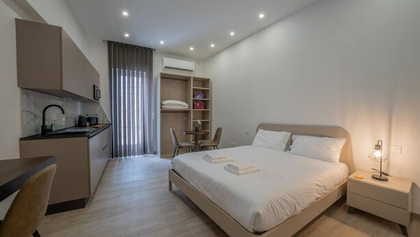 A modern hotel room with a bed, bedside table, and a desk area with a chair. - Urban Vibe 3 apartment (Kirkop)
