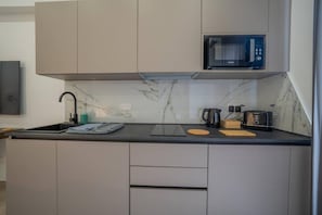 A modern kitchen with a built-in microwave, a kettle, a toaster, and a marble backsplash.