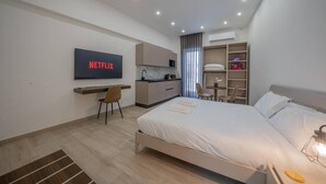 A modern hotel room with a bed, a desk, a TV displaying 'NETFLIX', a kitchenette, and a walk-in closet. - Urban Vibe 3 apartment (Kirkop)