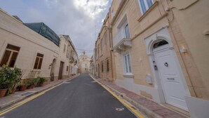 A narrow street lined with traditional buildings, featuring a clear sky and a few potted plants along the sidewalk. - Urban Vibe 3 apartment (Kirkop)