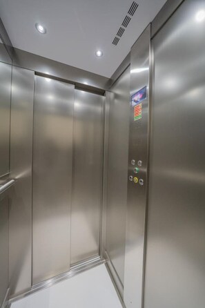 A metallic elevator interior with a control panel featuring buttons and a small sign.
