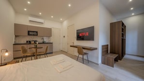 Ein modernes Hotelzimmer mit Bett, Schreibtisch, Fernseher, einer Küchenzeile und einem Kleiderschrank.