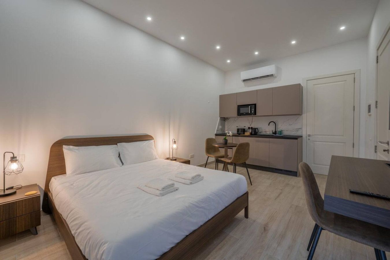 Une chambre d’hôtel moderne équipée d’un lit, de tables de chevet, d’un bureau, d’une chaise, d’un coin cuisine et d’un appareil de climatisation.
