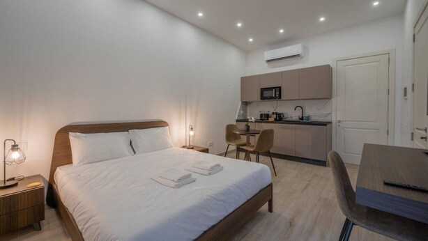 Ein modernes Hotelzimmer mit Bett, Nachttischen, einem Schreibtisch, einem Sessel, einer Küchenzeile und einer Klimaanlage.
