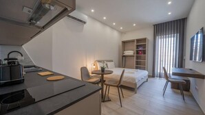 Ein modernes Hotelzimmer mit einer Küchenzeile, einem Bett, einem Schreibtisch und einem Fernseher.