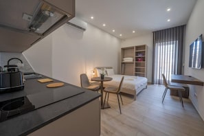 Una habitación de hotel moderna con kitchenette, una cama, un escritorio y un televisor.