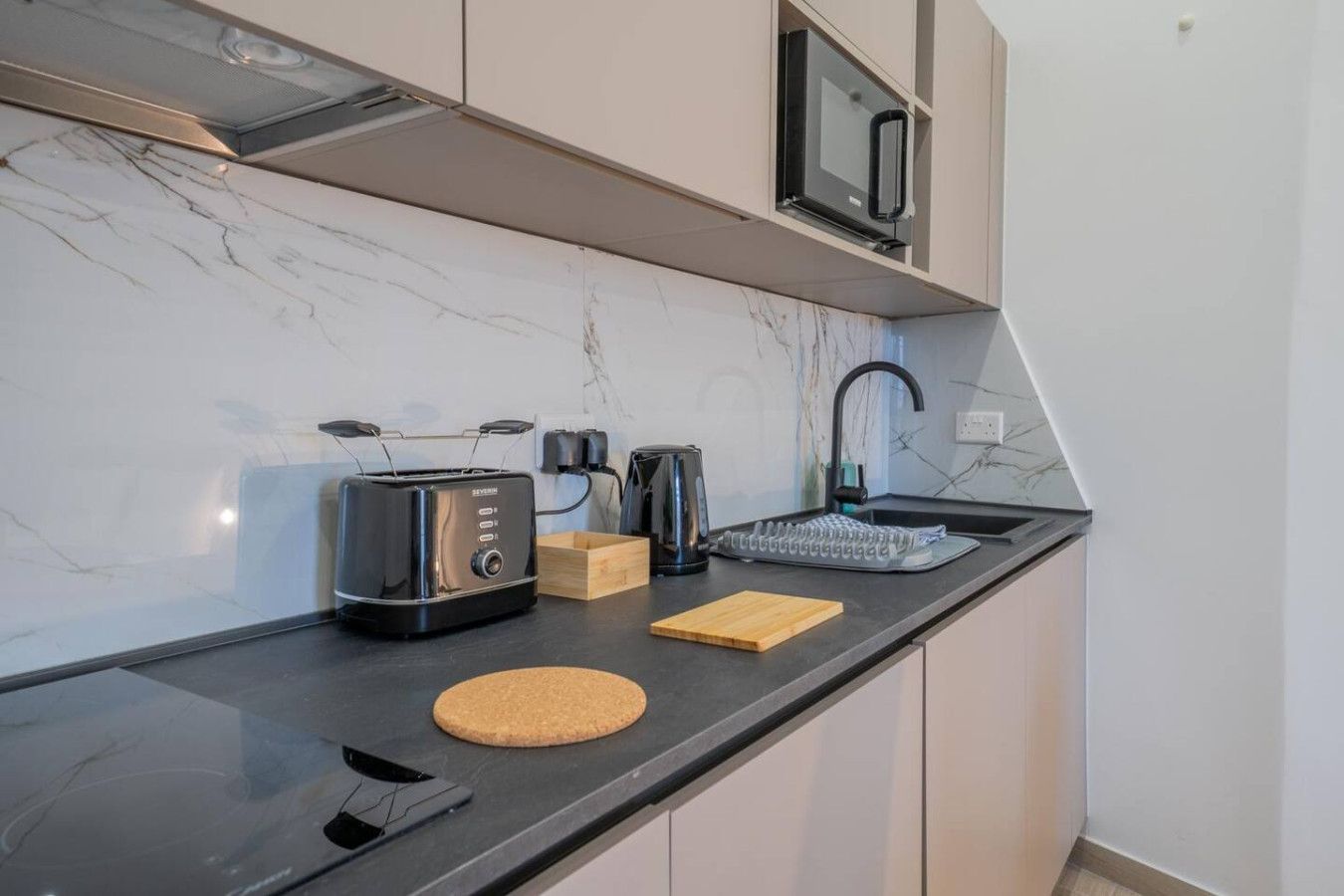 Una cocina moderna con encimera negra, un tostador, una tetera y un lavabo.