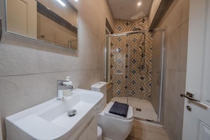 Un baño moderno con un lavamanos blanco, un inodoro y una zona de ducha con cerramiento de vidrio.