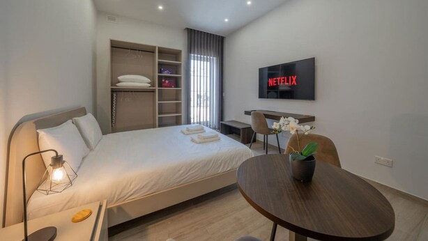 Ein modernes Hotelzimmer mit einem Bett, einem Schreibtisch, einem Fernseher und einem runden Tisch mit einer Pflanze.