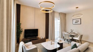 A modern living room with a flat-screen TV, a dining area with a round table, and a sofa. - Vanilla Homes Premium 1BR Yas Island (Abu Dhabi)