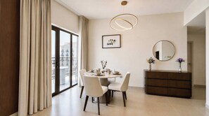 Un espace repas moderne avec une table ronde, des chaises, une commode et une grande fenêtre agrémentée de rideaux.