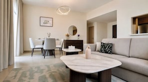 A modern living room with a sofa, a coffee table, and a dining area with chairs and a table. - Vanilla Homes Premium 1BR Yas Island (Abu Dhabi)