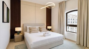 A hotel room with a large bed, two bedside lamps, a view of buildings through a window, and a modern light fixture above the bed. - Vanilla Homes Premium 1BR Yas Island (Abu Dhabi)