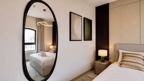 A hotel room with a bed, a nightstand with a lamp, a large mirror, and two framed artworks on the wall. - Vanilla Homes Premium 1BR Yas Island (Abu Dhabi)