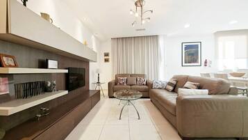 A modern living room with a sofa, a coffee table, and a TV on a wall-mounted shelf.
