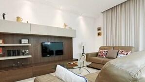 Ein modernes Wohnzimmer mit Ledersofa, Flachbildfernseher, Glastisch und einer Deckenleuchte.