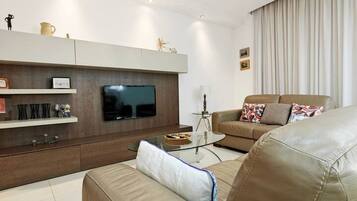 Ein modernes Wohnzimmer mit Ledersofa, Flachbildfernseher, Glastisch und einer Deckenleuchte.