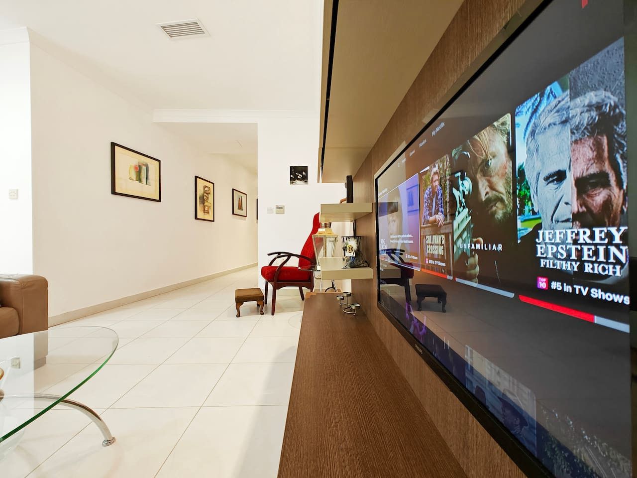 A modern lobby with a large TV screen displaying TV shows, a red chair, and framed artwork on the wall.