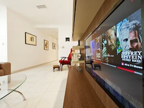 A modern lobby with a large TV screen displaying TV shows, a red chair, and framed artwork on the wall. - Good Times apartment (Sliema)