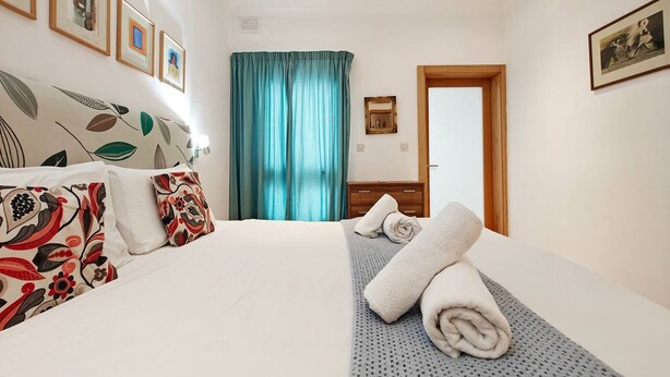 Ein Hotelzimmer mit Bett, Kissen, einem Handtuch, einem Vorhang und gerahmten Bildern an der Wand.