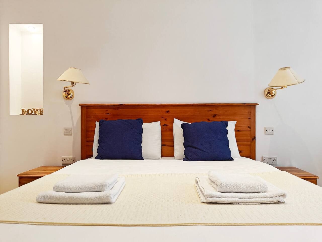 Ein Hotelzimmer mit einem hölzernen Kopfteil, zwei Nachttischlampen, einem Bett mit weißer Bettwäsche und einer Wandleuchte mit dem Wort 'LOVE'.