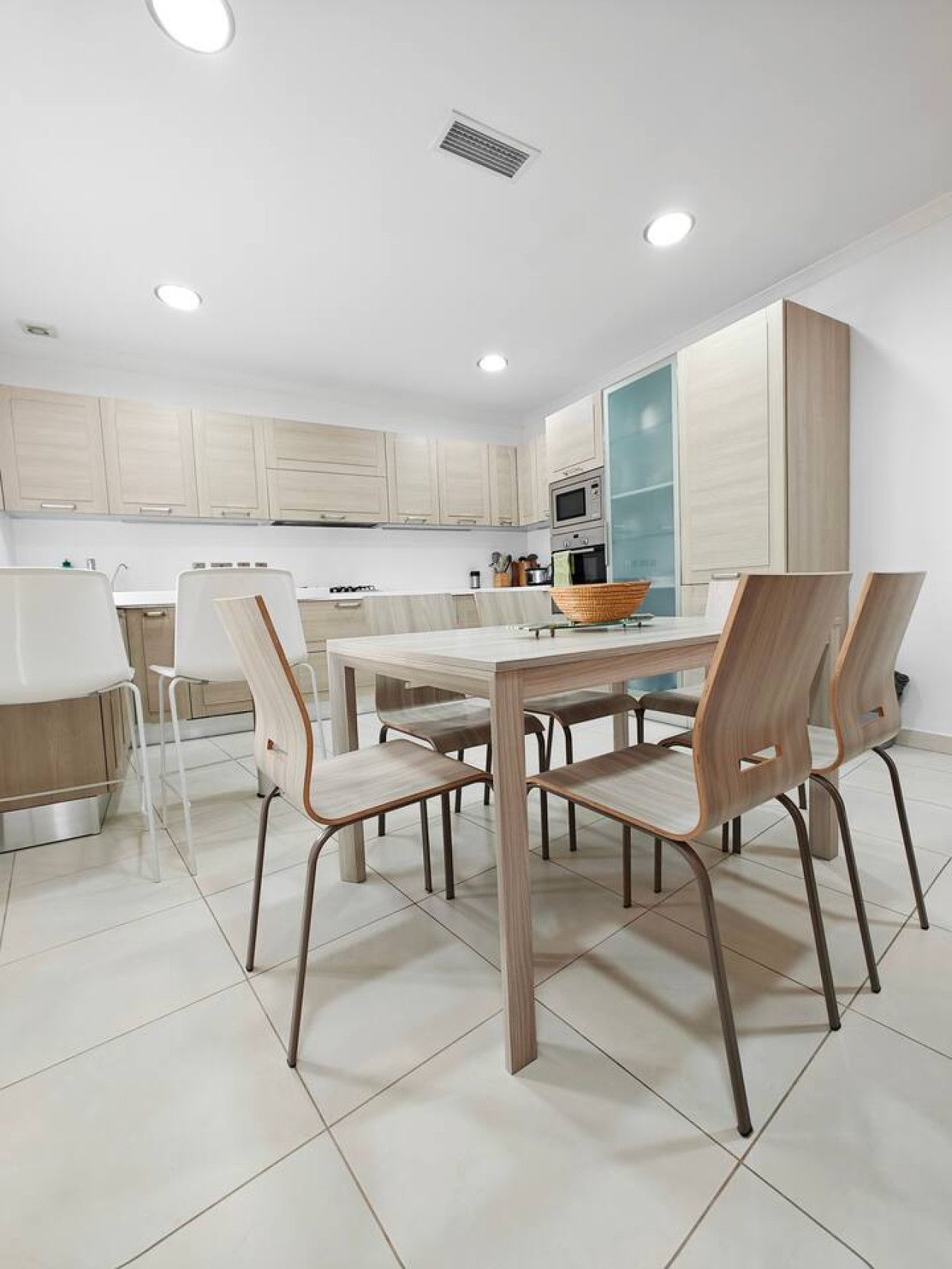 Una cocina moderna con armarios de madera clara, una isla central y un comedor con mesa y sillas.