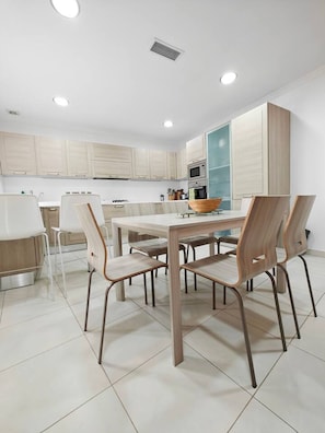 A modern kitchen with light wooden cabinets, a central island, and a dining area with a table and chairs. - Good Times apartment (Sliema)
