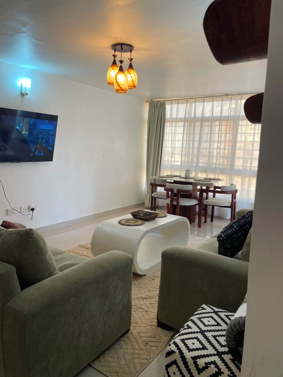 Een woonkamer met een flatscreen televisie, een eettafel met stoelen, een bank en een bijzondere witte salontafel.